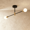 Clérachic 2-arm iron ring chandelier in black with brass sockets, frosted globe bulbs lit against a plaster ceiling.
