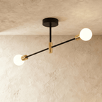 Clérachic 2-arm iron ring chandelier in black with brass sockets, frosted globe bulbs lit against a plaster ceiling.