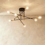 Clérachic 8-arm iron ring chandelier in black with brass sockets, clear filament bulbs lit against a plaster ceiling.