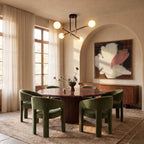 Clérachic 4-arm iron ring chandelier in black and brass, lit above a round dining table with green upholstered chairs.
