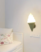 Green-coned Clérachic wall light lit beside a white daybed with a floral cushion and a wall socket plate on a pale wall.