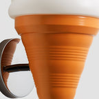 Close view of the ribbed orange cone on this Clérachic wall light, where it joins the curved chrome arm and round backplate.