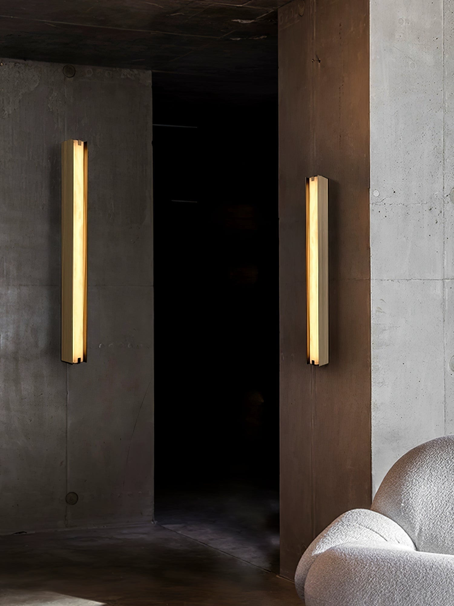 Clérachic Isolde sconces in pairs lighting a dark concrete passage beside a cream bouclé chair.