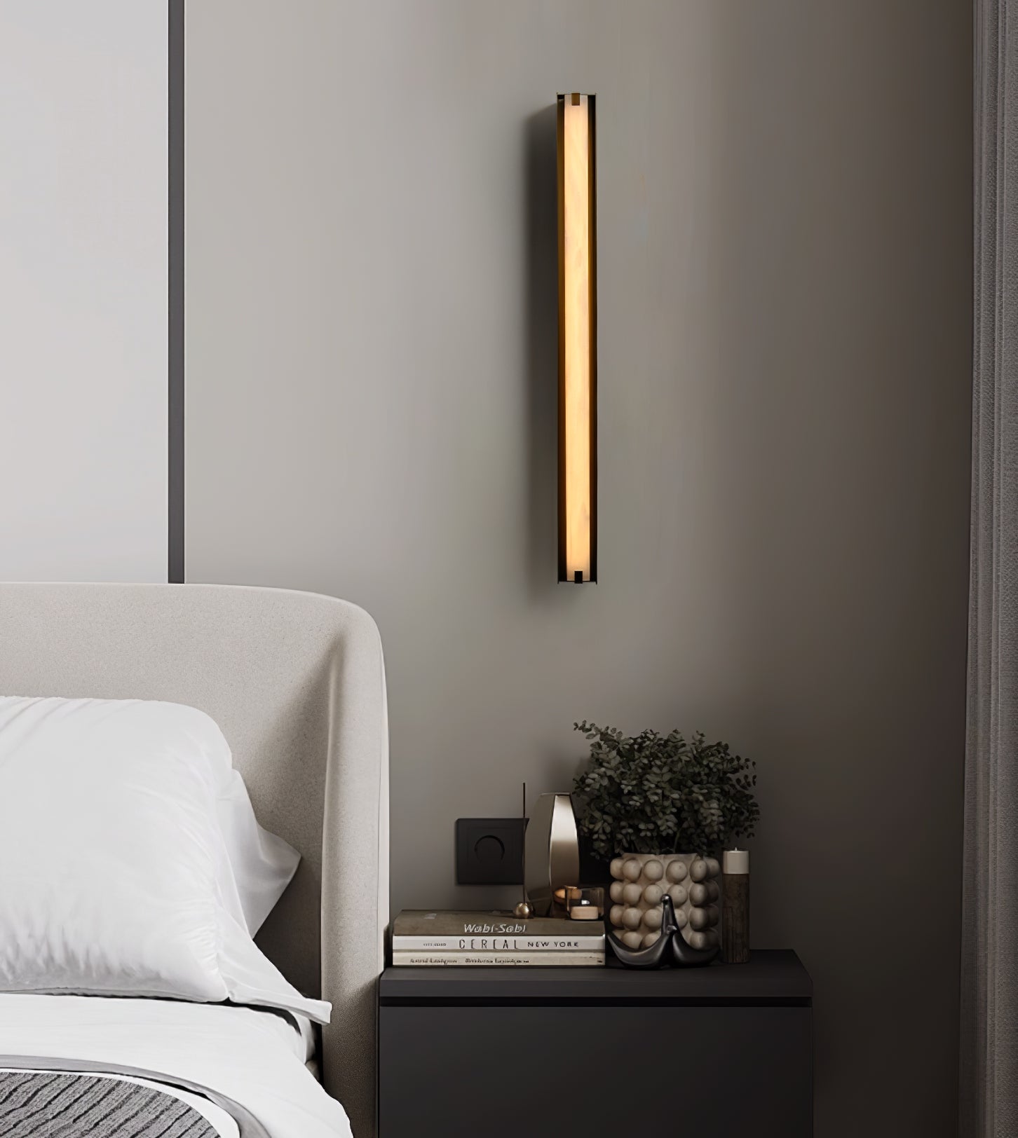 Clérachic Isolde beside an upholstered bed, its warm column of light falling over a dark nightstand.