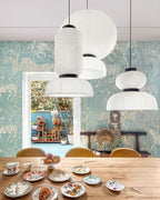 Clérachic paper pendant lamps above a wooden table laid with patterned china, against leafy wallpaper by an open garden door.
