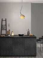 The Clérachic Ivvaros pendant over a dark kitchen island, its small shade lit warm against a pale wall.