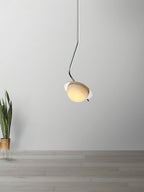 The Clérachic Ivvaros pendant against a plain wall, chrome stem hooking the alabaster shade forward.