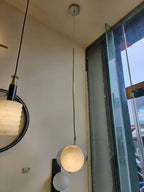 Clérachic Ivvaros hung beside a window, its lit alabaster shade catching daylight off the glass.