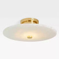 Clérachic brass flush mount from a lower angle, the stone shade glowing around a small brass centre cap.
