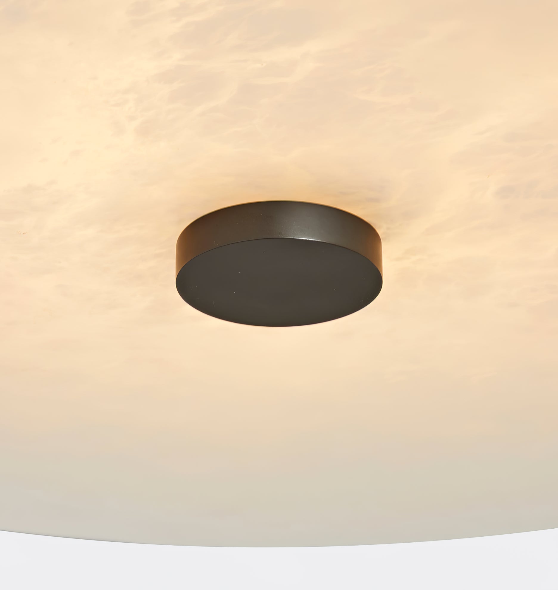 Clérachic alabaster up close, a black centre cap set into softly glowing, cloud-patterned natural stone.