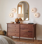 Clérachic fixtures grouped around an arched brass mirror above a walnut dresser in a warm bedroom.