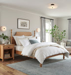 The Clérachic light on the ceiling with two more flanking the bed, filling a calm oak and linen bedroom.