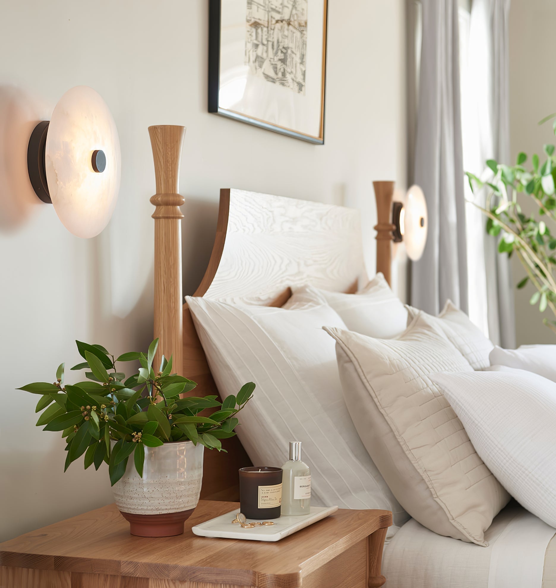 Clérachic fixtures in black and brass set either side of a bed, glowing over linen pillows and a potted plant.