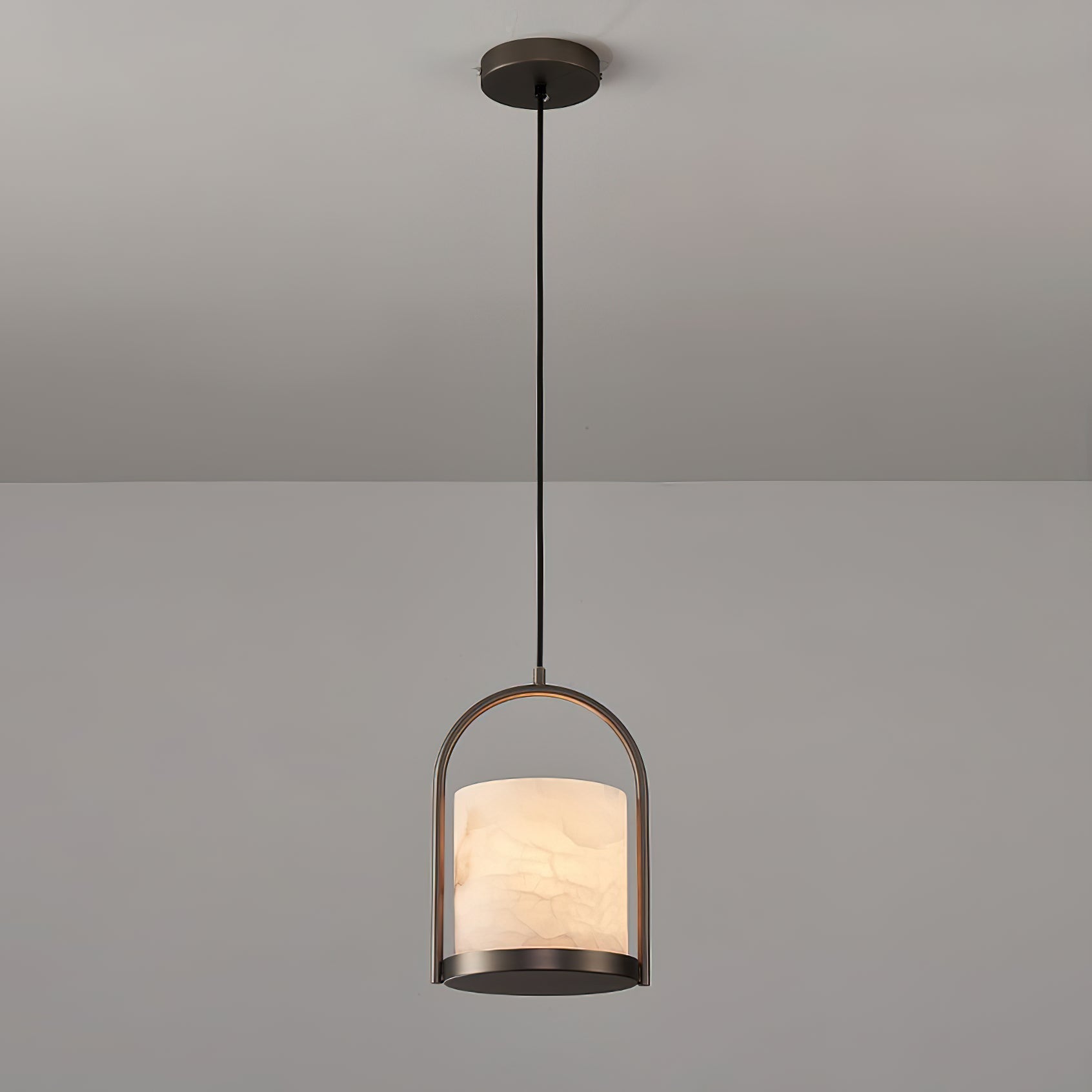 Lit against a soft grey wall, the Clérachic Jewel Pendant Light glows through its alabaster shade above the dark base disc.