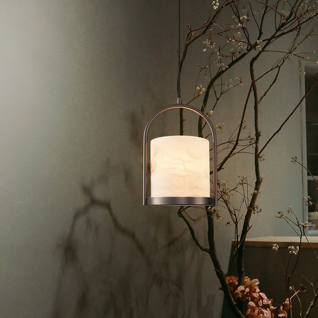 Clérachic Jewel Pendant Light lit low over a console, its alabaster shade warm against a dark plaster wall and bare branches.