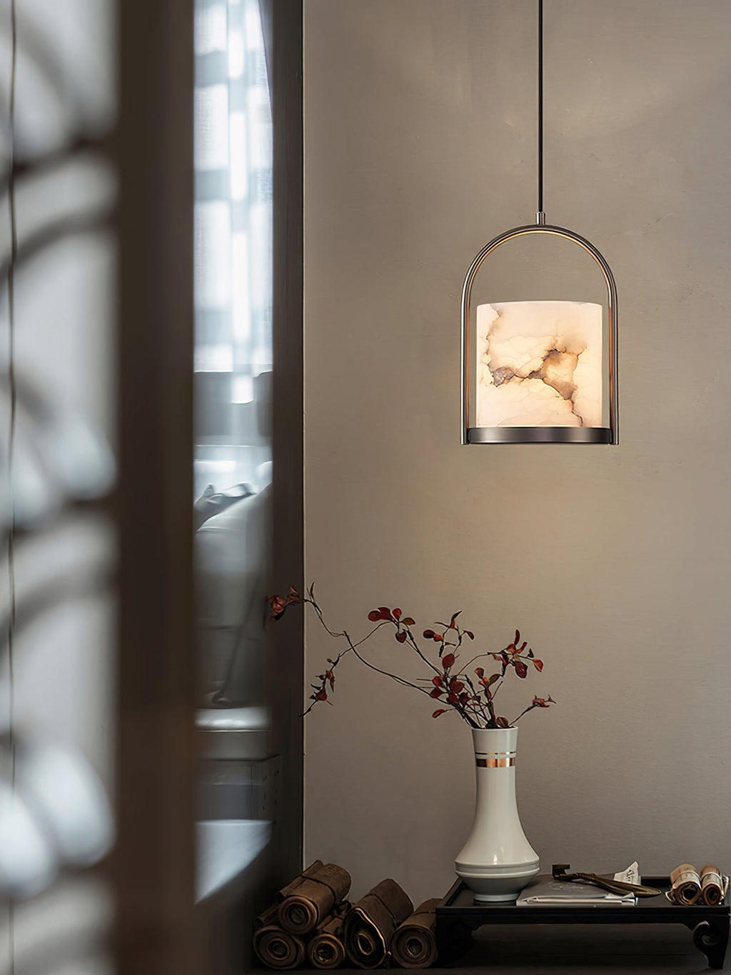 Clérachic Jewel Pendant Light glowing next to a window screen, hung above a console with a vase of red-leafed stems.