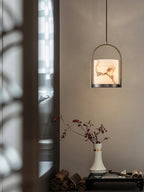 Clérachic Jewel Pendant Light glowing next to a window screen, hung above a console with a vase of red-leafed stems.