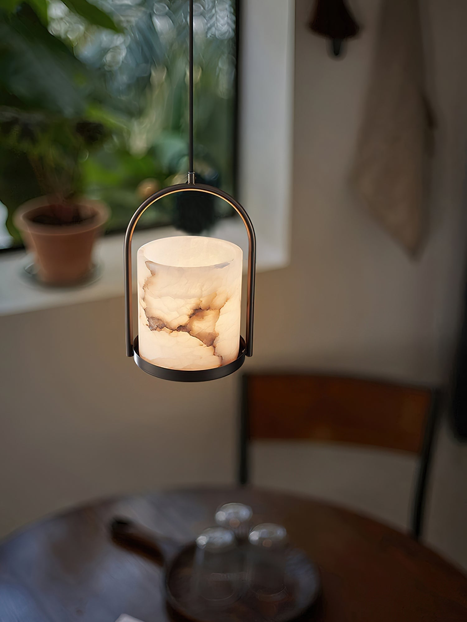 Close view of the Clérachic Jewel Pendant Light lit above a wooden table, alabaster veining showing through the warm glow.