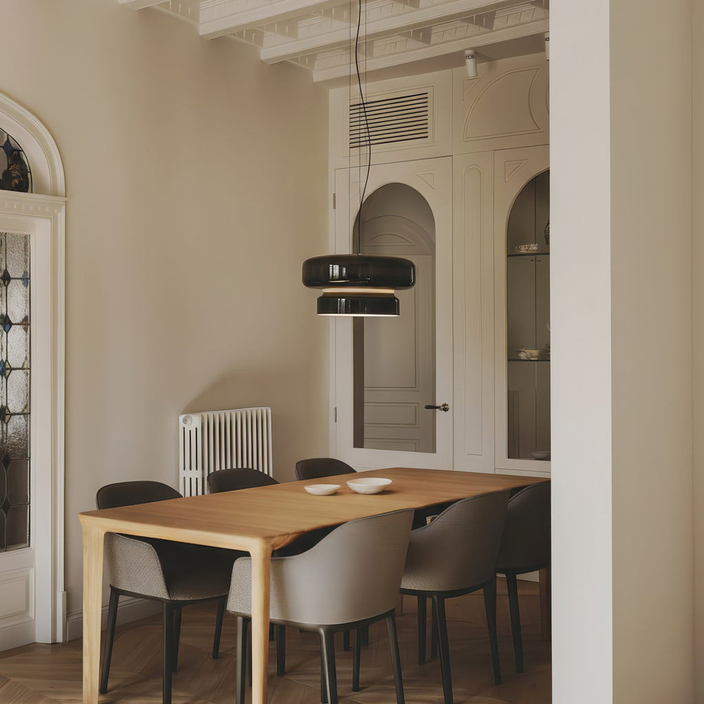 This Clérachic glass pendant hangs over a pale wood dining table with grey chairs, in a room with an arched door and a radiator.