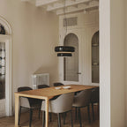 This Clérachic glass pendant hangs over a pale wood dining table with grey chairs, in a room with an arched door and a radiator.