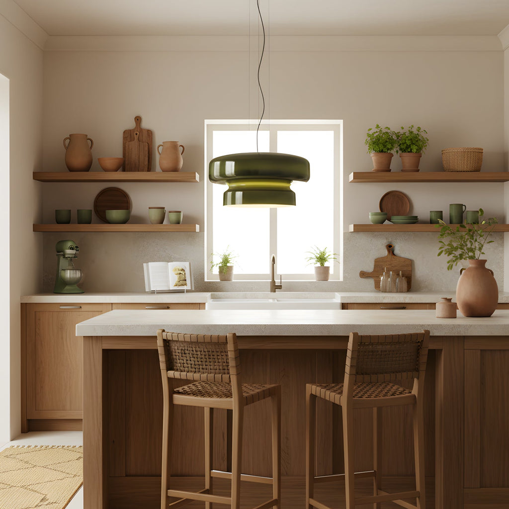 Clérachic green glass pendant in front of a sunlit window in a kitchen, with wooden stools at an island and clay pots on open shelves.