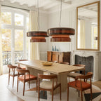 Two Clérachic Amber Red glass pendants hang above a long pale table with russet chairs, in a room with tall windows and a gilt mirror.