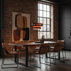 A Clérachic Amber Red glass pendant glows beside a tall window in a brick-walled dining room, above a dark table with leather chairs.