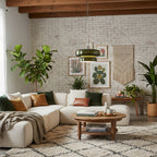 A Clérachic dark green glass pendant hangs in a living room with a cream corner sofa, a brick wall and framed botanical prints.