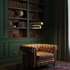 Clérachic dark green pendants glow above a leather armchair, in a dark green panelled corner with a shelf of books.