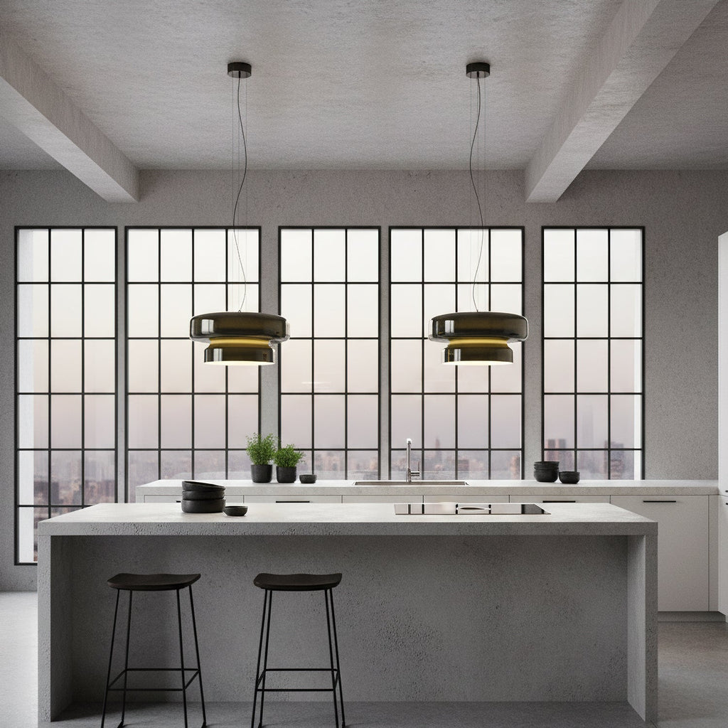 Two Clérachic dark glass pendants hang above a grey kitchen island with black stools, in front of a wall of grid-pane windows.
