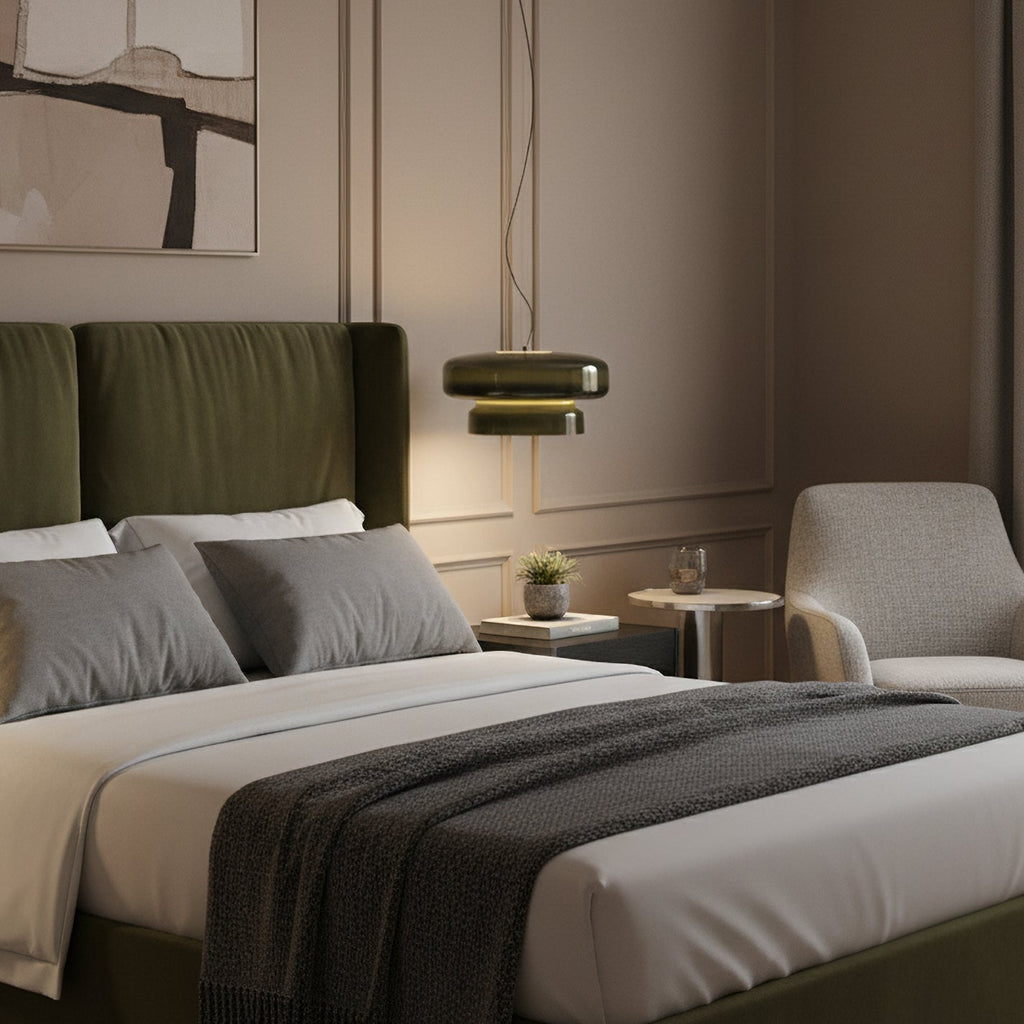 A Clérachic dark green glass pendant hangs beside a bed with a green headboard, grey bedding and a small side table.