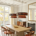 Close view of two Clérachic Amber Red glass pendants glowing in a bright dining room with tall windows and a gilt mirror.