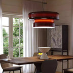A Clérachic Amber Red glass pendant with a bright orange band, hung close to a tall window with sheer curtains and a table below.