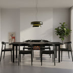 Clérachic dark green glass pendant above a long black table with black chairs, with a fireplace, a plant and a print behind.