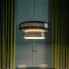 A Clérachic smoky green glass pendant glowing between deep green velvet curtains, with a blue-green panelled wall behind.