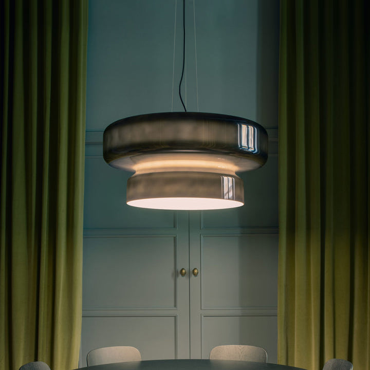 A Clérachic smoky green glass pendant glowing between deep green velvet curtains, with a blue-green panelled wall behind.