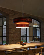 A Clérachic Amber Red glass pendant over a long timber table with small glass vases, with arched windows behind.