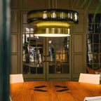 Close view of a lit Clérachic dark green glass pendant above a round wooden table, with glass-panelled doors behind.