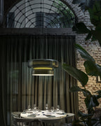A Clérachic green glass pendant in a dark courtyard dining room, with sheer curtains, a brick wall and a table set for dinner.