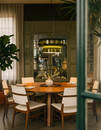 A lit Clérachic green glass pendant above a round table with white chairs, framed by a doorway and leaves, in an olive room.