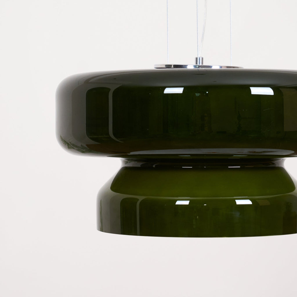 A Clérachic dark green glass pendant with a chrome top plate and fine cords, seen close up against a pale backdrop.