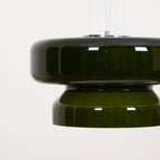 A Clérachic dark green glass pendant with a chrome top plate and fine cords, seen close up against a pale backdrop.