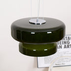 Close view of the Clérachic dark green pendant, with its chrome plate, wide glass disc and stepped lower tier, above a printed poster.