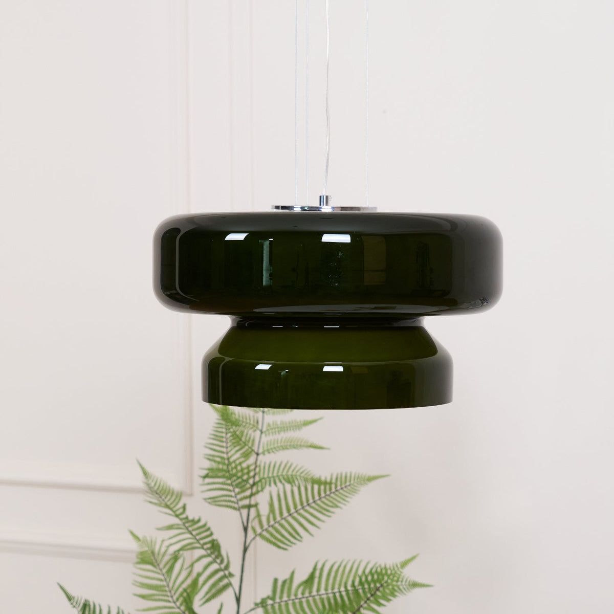 A Clérachic dark green glass pendant above a fern and a white table with a few small orange stems.