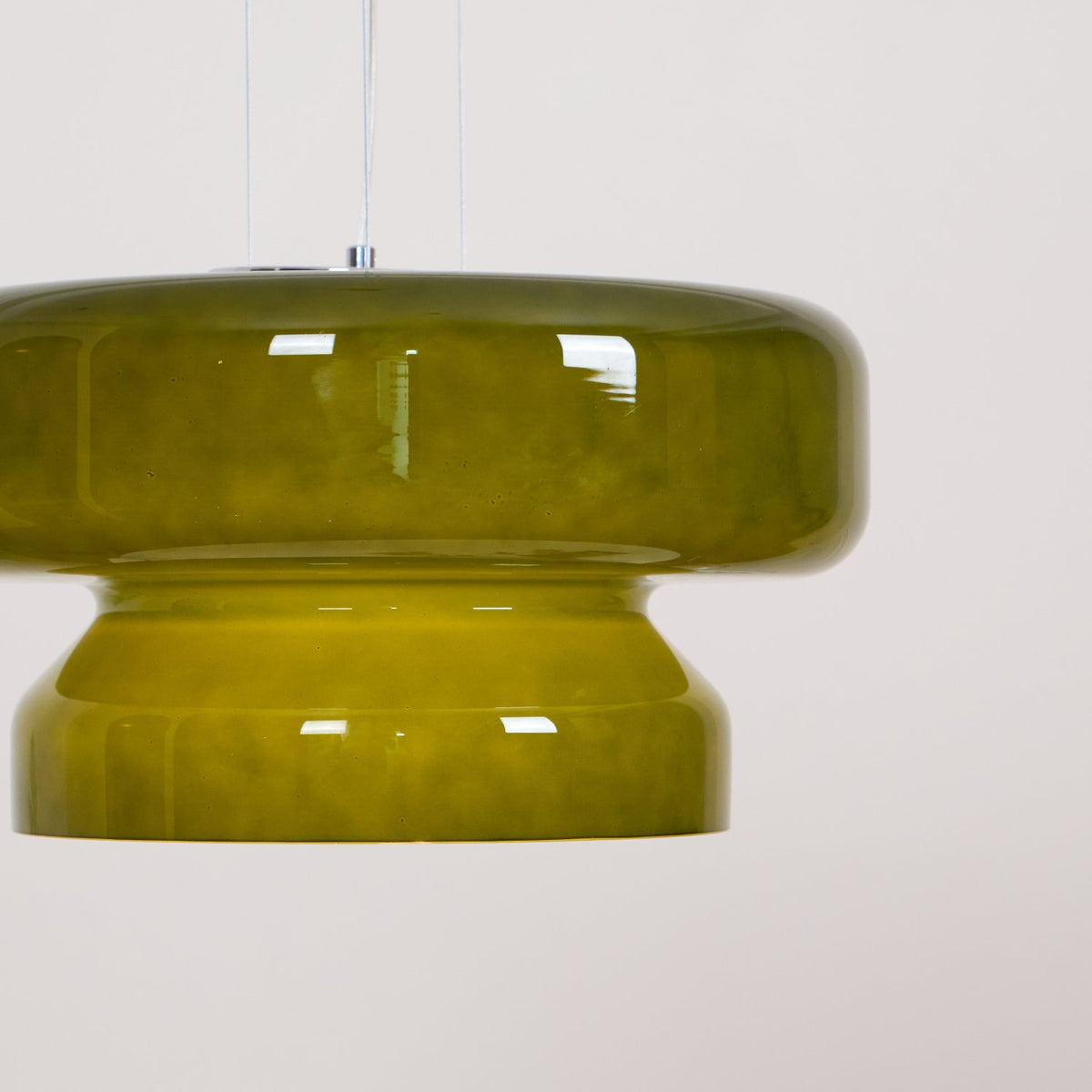 Close view of a Clérachic olive-green glass pendant, with its wide upper disc and narrower stepped base.