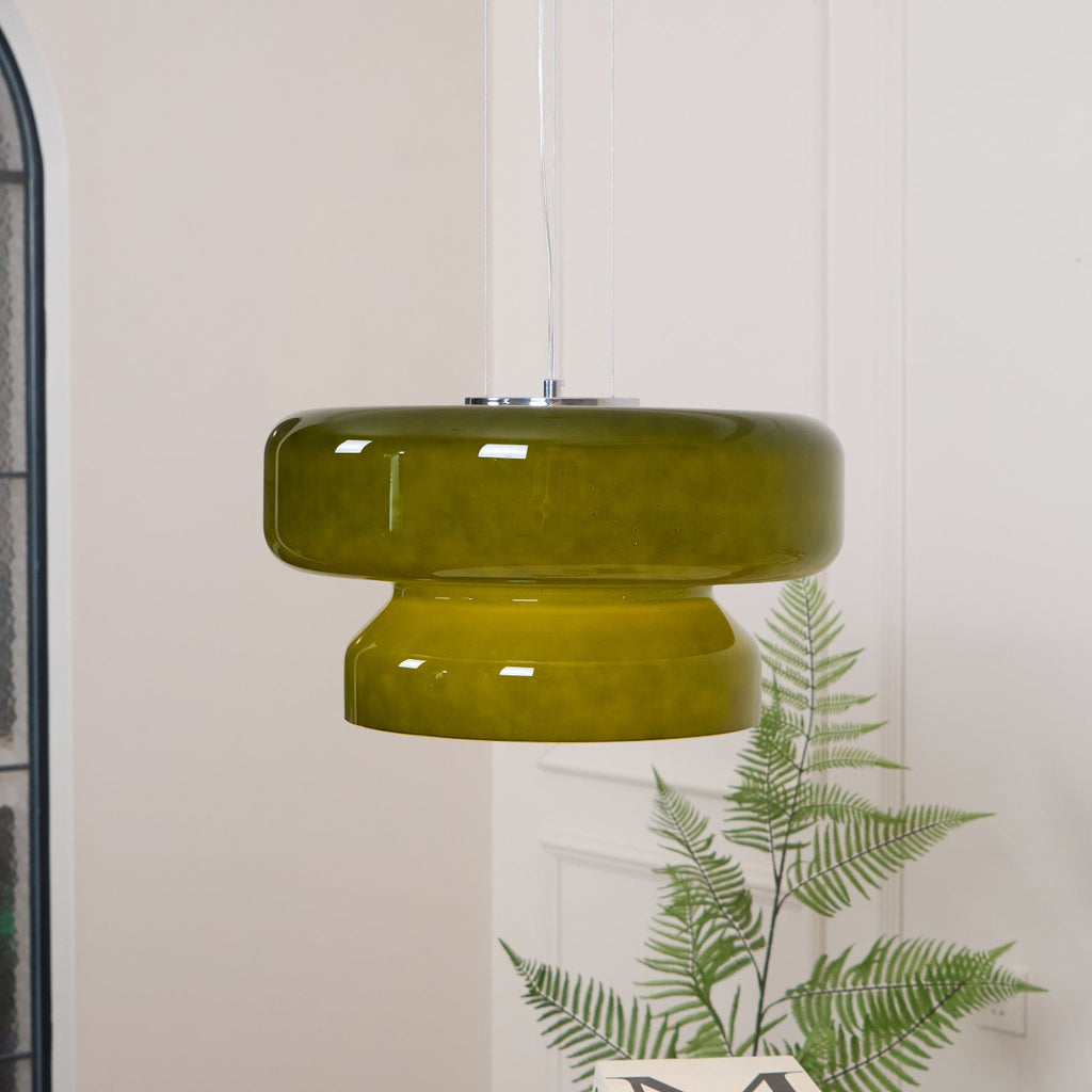 A Clérachic olive-green glass pendant with a chrome plate, above a fern and a white table.