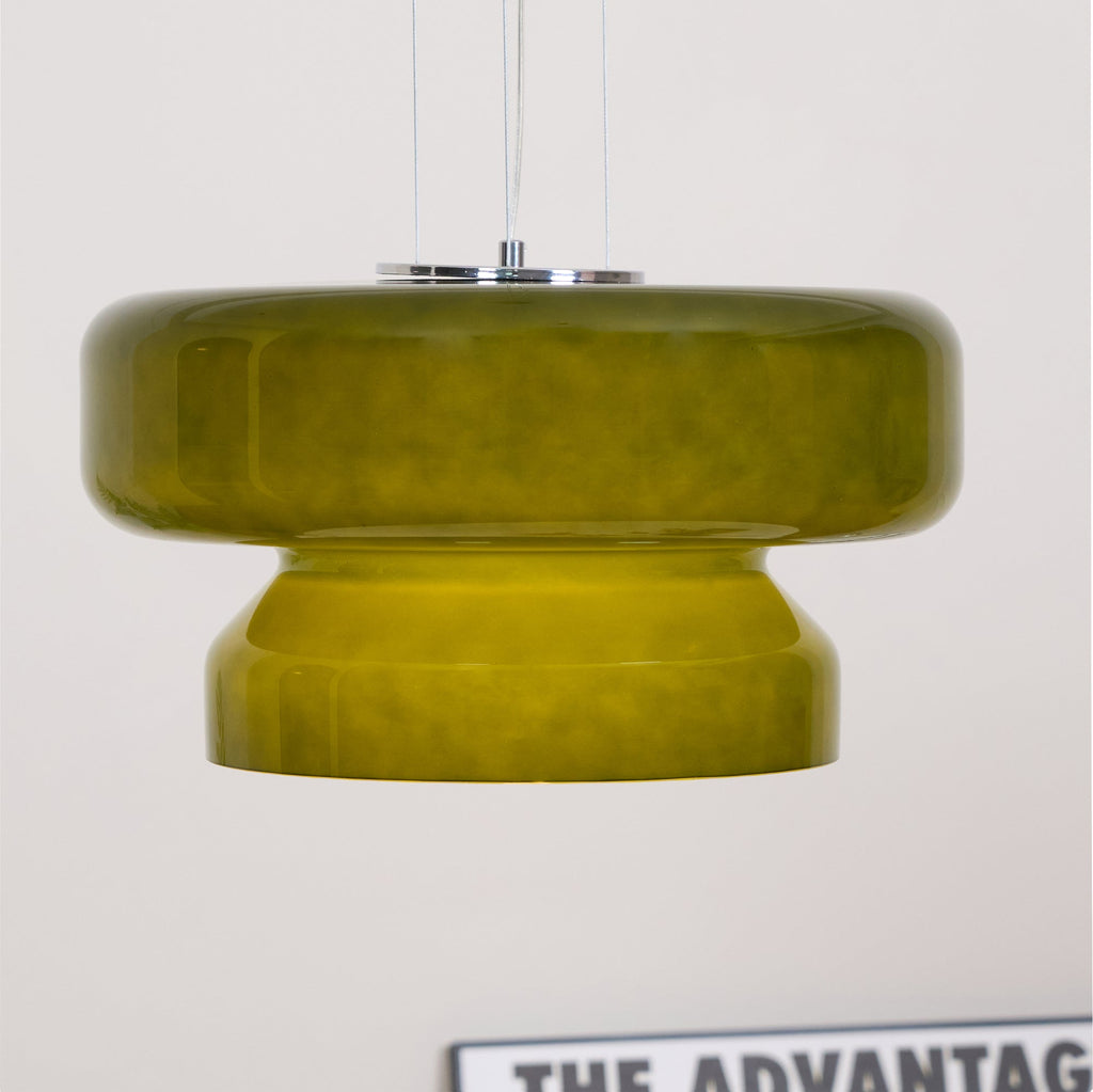 Close view of a Clérachic olive-green glass pendant against a white wall, with a poster edge at the bottom.