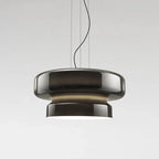 A Clérachic pendant in smoky brown-grey glass, with a soft beige glow between its two tiers, on a pale grey backdrop.