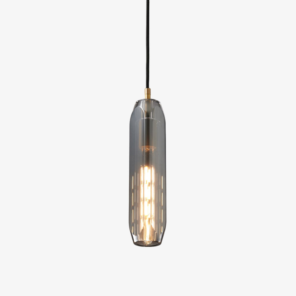 A tall Clérachic pendant with a smoke grey glass shade and a brass top, lit with a filament bulb, on a plain white backdrop.
