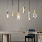 Six Clérachic pendants in different glass shapes hang at varied heights above a marble dining table and a navy chair.